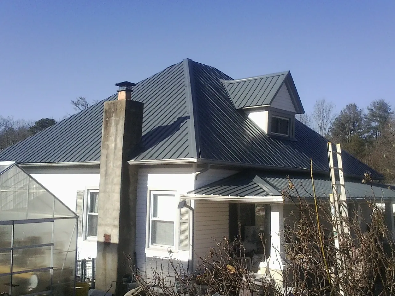 Dark blue standing seam metal roof on a white farmhouse with dormer — Slate & Tile Roof Repair by Roofing Brothers in Claremont