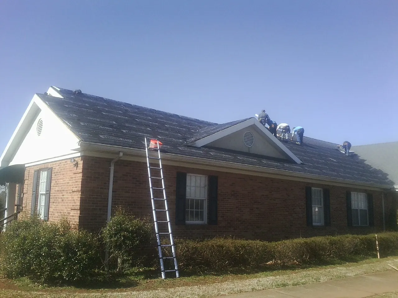 Crew tearing shingles off a brick ranch roof with a ladder set — Emergency Roof Repair work by our crew in Claremont
