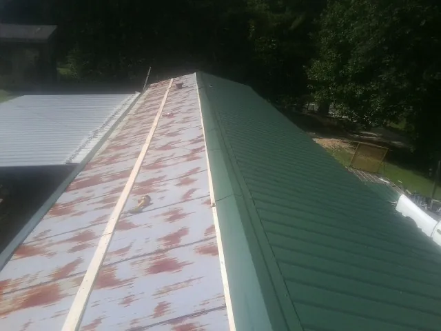 Old rusted panels beside newly installed green metal roofing — Wind Damage Roof Repair by Roofing Brothers in Claremont