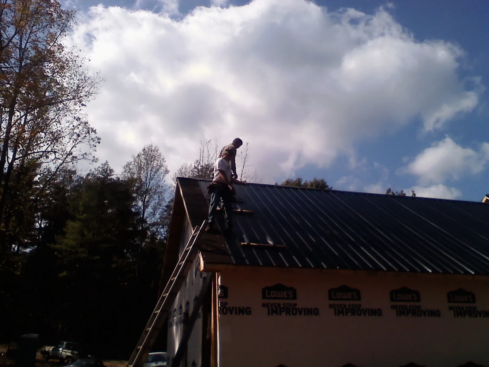 Roofer fastening dark metal panels high against a cloudy sky, from a Roof Inspection job in Claremont